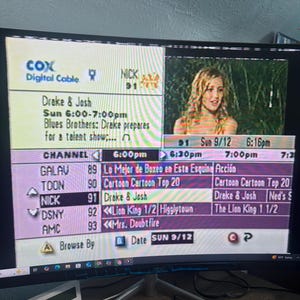 以下が含まれることがあります： Cox Digital Cableのロゴが表示されたテレビ番組表を映すコンピューターモニター。Nickなどのチャンネルの番組がリスト表示され、「Drake & Josh」がハイライト表示されています。小さな白いデバイスが手前にあります。日付は9/12（日）です。
