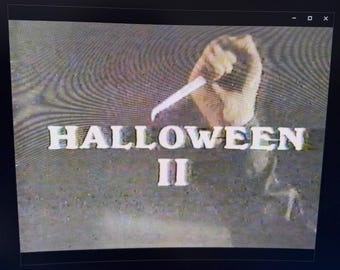 Könnte beinhalten: Ein Filmbild von Halloween II. Der Titel ist in weißen Blockbuchstaben geschrieben. Eine Hand, die ein Messer hält, ist zu sehen. Der Hintergrund hat eine körnige Textur und eine dunkle Farbpalette.