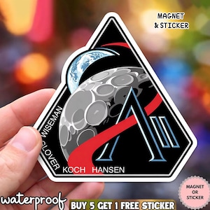 Może przedstawiać: Czarna, biała i czerwona naklejka lub magnes z wystylizowanym wzorem księżyca i Ziemi. Projekt zawiera literę "A" oraz nazwiska "WISEMAN", "GLOVER", "KOCH" i "HANSEN". Widoczne są również słowa "MAGNET & STICKER" i "waterproof".