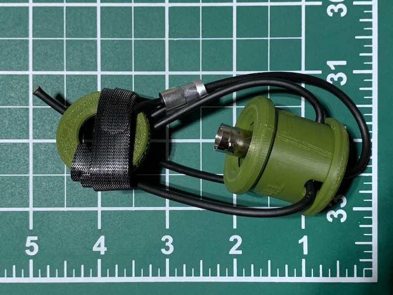 May include: A green and black cable connector with a black strap. The connector has a silver metal tip and a black wire attached to it.