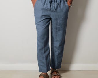 Puede incluir: Pantalones de lino azul claro con cintura con cordón. Los pantalones tienen un corte relajado y se combinan con sandalias marrones. El modelo lleva una camisa abotonada de color claro. Los pantalones son de color liso y parecen estar hechos de una tela ligera.