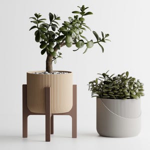 May include: Two decorative planters with greenery. One is a beige, ribbed pot on a brown stand. The other is a smaller, gray, ribbed pot. Both pots contain green plants. The background is white.