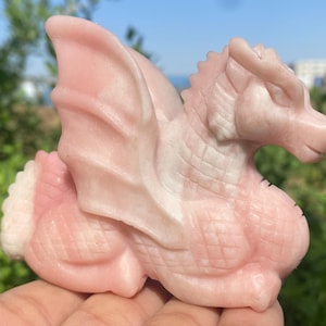 May include: A pink dragon sculpture carved from rose quartz. The dragon is curled up with its wings spread out.