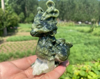 Op de afbeelding: Een gebeeldhouwd jade beeldje van een mythisch wezen, in groen en wit. De sculptuur heeft gedetailleerde kenmerken, waaronder een kop met hoorns en een lichaam met afgeronde vormen. Het beeldje wordt in een hand gehouden.