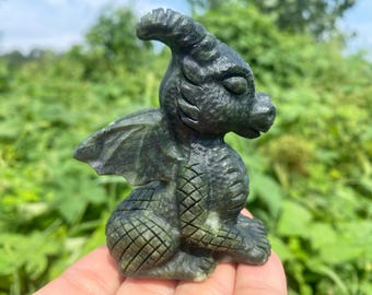 Op de afbeelding: Een gedetailleerd, donkergroen drakenbeeldje met getextureerde schubben, vleugels en hoorns. De draak zit, met zijn vleugels iets gespreid. De sculptuur staat tegen een vage groene achtergrond.