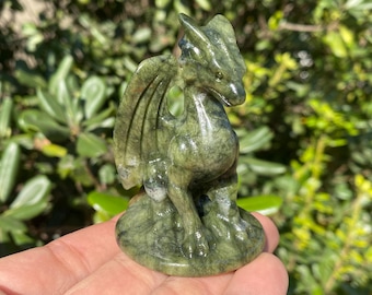 May include: A detailed, green dragon figurine carved from stone. The dragon has large wings, a long neck, and a detailed face. The figurine is approximately 4 inches tall and sits on a round base. The dragon is a mythical creature.