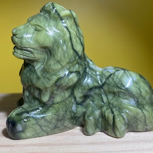 Puede incluir: Escultura de león de mármol verde con detalles intrincados. El león está sentado con la cabeza girada hacia un lado.