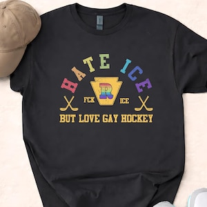 May include: Black t-shirt with the text "HATE ICE BUT LOVE GAY HOCKEY" in rainbow colors. The design includes hockey sticks and a Pennsylvania keystone shape with a rainbow "R". A tan baseball cap and white sneakers are also visible.