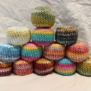 May include: A pyramid stack of twelve round, crocheted hacky sacks. Each ball features a unique color combination, including variegated yarns in shades of blue, yellow, pink, green, orange, and brown, all crafted with a consistent textured stitch.