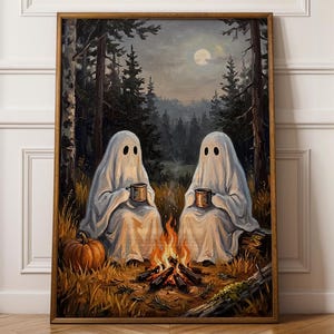 Könnte beinhalten: Ein gerahmter Wandkunstdruck, der zwei weiße Geisterfiguren zeigt, die nachts in einem dunklen Wald sitzen. Die Geister halten Tassen an einem kleinen Lagerfeuer, daneben liegt ein Kürbis. Die Szene zeigt hohe Kiefern und einen Vollmond am Himmel.