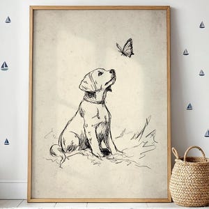 Può includere: Una stampa incorniciata con un disegno a penna e inchiostro di un cucciolo di Labrador Retriever che guarda una farfalla. L'opera d'arte ha un'estetica vintage, con uno sfondo beige chiaro e una semplice cornice in legno. La stanza è decorata con adesivi murali a tema nautico.