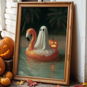 Op de afbeelding: Een ingelijst Halloween-kunstwerk toont een spook op een flamingo-zwemband met een pompoen-lantaarn. Verschillende uitgesneden pompoenen met oplichtende gezichten en herfstbladeren zijn gerangschikt op een houten oppervlak, wat een feestelijke herfstscène creëert.