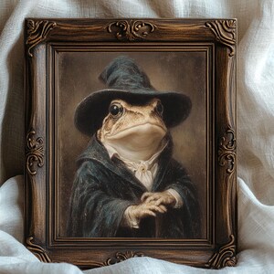 May include: A framed portrait of a frog dressed in a dark blue witch's hat and coat, with a white shirt and a serious expression. The ornate, dark brown frame adds a vintage aesthetic to the artwork.