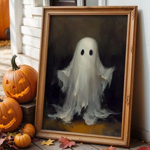 Może przedstawiać: Oprawiony obraz białego ducha z czarnymi oczami, wystawiony na drewnianym ganku. Wyrzeźbione pomarańczowe dynie z podświetlonymi twarzami i jesienne liście otaczają obraz, tworząc motyw Halloween.