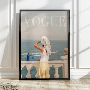May include: A framed wall art print featuring a magazine cover titled VOGUE SUMMER EUROPE. The image shows a person with a white towel wrapped around their head, wearing a white tank top and yellow pants, standing on a balcony overlooking the sea.