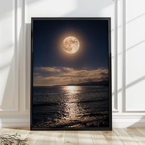 May include: A framed vertical wall art print featuring a night scene of a full moon glowing in a dark starry sky above a calm ocean. The moonlight reflects on the water surface, with a distant dark coastline visible beneath a layer of clouds.