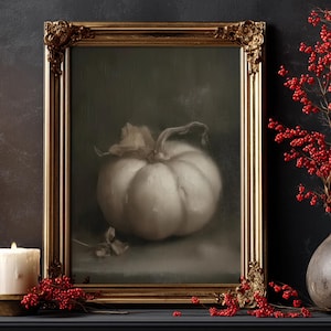 Puede incluir: Pintura enmarcada de una calabaza blanca con tallo y hojas, en un marco dorado ornamentado. Bayas rojas y una vela en primer plano, sobre un fondo oscuro.