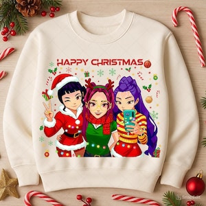 Puede incluir: Sudadera color crema con un diseño festivo. El gráfico presenta tres personajes de estilo anime vestidos con atuendos navideños, tomándose una selfie. Las palabras "HAPPY CHRISTMAS" están impresas encima de los personajes. Decoraciones navideñas rodean la imagen.