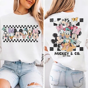 May include: White sweatshirt featuring a graphic of Disney characters, including Mickey Mouse, Donald Duck, and Goofy. The front design is a row of character faces above a black and white checkered pattern. The back features a group of characters with "Mickey & Co. EST 1928".