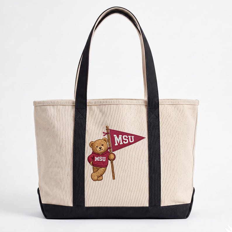 May include: Cream-colored tote bag with black handles and base. The bag features an embroidered design of a teddy bear wearing a maroon sweater and holding a maroon pennant with "MSU" in white letters. The bag is made of canvas.