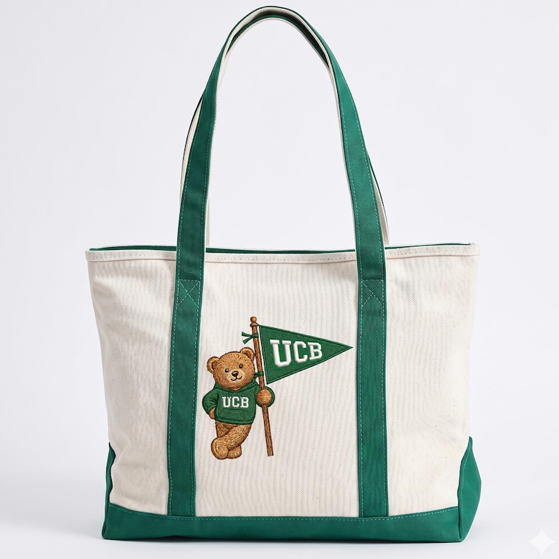 May include: Cream-colored tote bag with green accents and handles. Features a brown bear wearing a green hoodie with "UCB" embroidered on it, holding a green flag with "UCB" on it. The bag is made of canvas-like material.