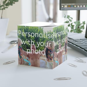 Puede incluir: Un bloc de notas blanco en forma de cubo con una foto de un hombre que sostiene a dos niños. El bloc de notas tiene el texto "Personaliza con tu foto" en la parte delantera.