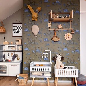 May include: A white wooden doll crib with a doll inside, a white wooden changing table with a doll inside, and a wooden shelf with a bunny rabbit and other toys. The wall is covered in a green and blue wallpaper with a pattern of houses and flowers. The text "Good Night" is on a black and white sign on the wall.