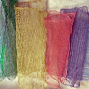 May include: A collection of colorful, sheer fabric strips in shades of purple, green, gold, red, purple, and blue. The fabric has a textured, open weave, and is arranged side by side. The colors are vibrant and the fabric appears lightweight.