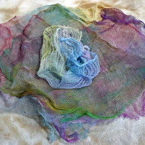 May include: A piece of sheer, lightweight fabric with an open, loose-weave mesh texture. The material features a multi-coloured gradient pattern, blending shades of blue, green, purple, yellow, and pink throughout the irregular, flowing edges.