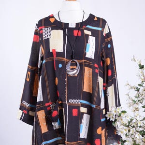 May include: A black tunic top with a colourful geometric pattern in orange, red, white, and blue. The top has three-quarter sleeves and a round neckline. A silver pendant necklace hangs from the neckline.