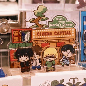 May include: Acrylic charms featuring anime-style characters and building designs. The charms include a tree, a restaurant sign that says "Maria's Dinner", and a cinema sign that says "Cinema Captial".