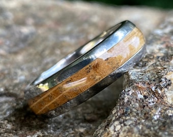 Puede incluir: Un anillo de plata con una incrustación de madera marrón. La madera tiene un patrón de veta natural y está encapsulada en resina transparente.
