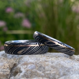 Może przedstawiać: Dwa srebrne obrączki ślubne z cienkim wkładką ze złota. Obrączki mają fakturowane, szczotkowane wykończenie.