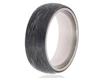 May include: A black and silver ring with a textured carbon fiber band. The ring is made of titanium and has a polished finish.