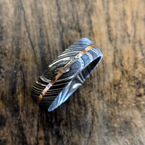 May include: A silver and rose gold wedding band with a patterned design. The band is made of metal and has a polished finish.