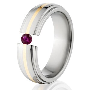 May include: A silver and gold wedding band with a single ruby gemstone set in the center. The band has a grooved design and a polished finish.