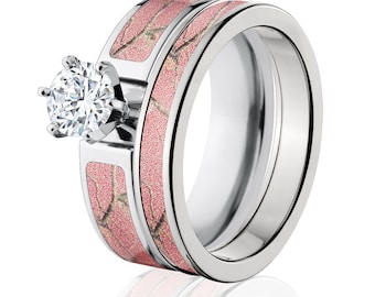 Op de afbeelding: Een set van twee trouwringen met een roze camouflagepatroon. De grotere ring heeft een enkele ronde diamant in het midden.