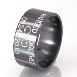 May include: A black metal ring inscribed with the words "Banded Together" and a stylised fish hook design, along with the date "09.24.2013".