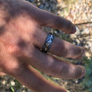 May include: A silver and rose gold band with a hammered finish. The band has a unique pattern and is worn on a finger.