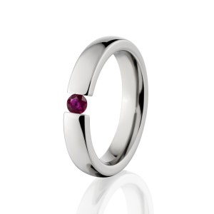 Può includere: Un anello d'argento con un'unica pietra preziosa di rubino incastonata nella fascia.