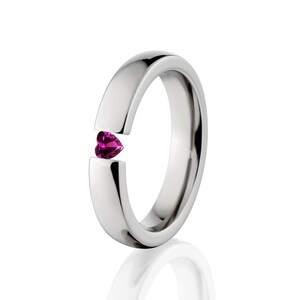 May include: A silver band with a heart-shaped pink gemstone set into the side.