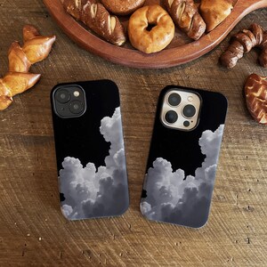 Könnte beinhalten: Zwei schwarze Handyhüllen mit einem weißen Wolken-Design. Die Hüllen haben einen Kamera-Ausschnitt und sind aus hartem Kunststoff.