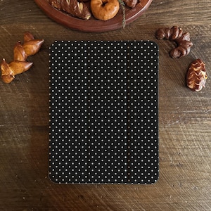 Può includere: Una custodia nera per tablet con un motivo a pois bianchi. La custodia è rettangolare con angoli arrotondati. Lo sfondo è una superficie di legno con prodotti da forno, tra cui pretzel e una ciambella.