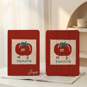 May include: Two red tablet cases with a tomato design. Each case features a cartoon tomato with a green stem and the word "TOMATO" below. One case has a signature in the bottom corner.