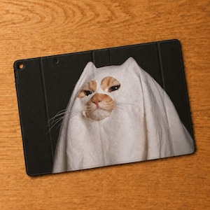 May include: A black tablet case featuring a graphic print of an orange cat wearing a white ghost costume. The cat's face is visible through two eye holes in the fabric, with long white whiskers extending from the sides of the ghost sheet.