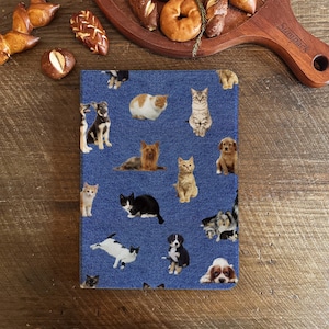 Könnte beinhalten: Ein blauer Jeansstoff mit einem sich wiederholenden Muster aus Katzen und Hunden. Der Stoff zeigt eine Vielzahl von Rassen und Farben von Katzen und Hunden.