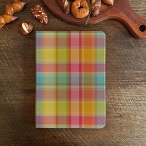 Könnte beinhalten: Ein Notizbuchumschlag mit einem farbenfrohen Karomuster in Rosa, Gelb, Orange und Blau. Das Notizbuch ist rechteckig mit abgerundeten Ecken. Der Hintergrund ist eine Holzoberfläche mit Backwaren.