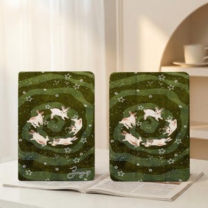 May include: Two green tablet cases with a whimsical design. Each case features a spiral pattern with white stars and a circle of white rabbits. The cases have the signature "Zoey" in the bottom corner.