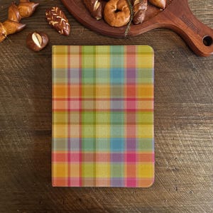 May include: A rectangular object with a vibrant plaid design in shades of pink, orange, yellow, green, and blue. It rests on a dark wooden surface, with various baked goods visible in the background.