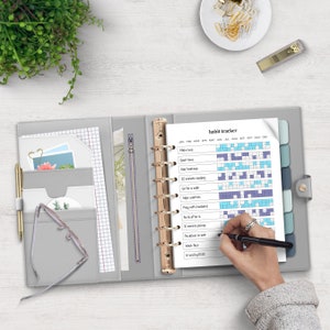 May include: A gray leather bound planner with gold rings and a habit tracker page. The habit tracker page has a list of habits to track, including "Make bed", "Quiet time", "20 minutes reading", "Go for a walk", "Wipe counters", "Pray with husband", "No to after 6", "10 minutes pickup", "No dishes in sink", "Wash face", "In bed by 10:30".
